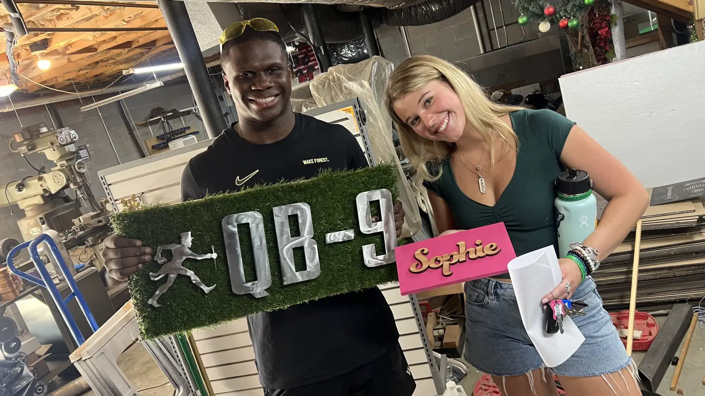 Two makers smiling and holding their finished custom signs in a workshop