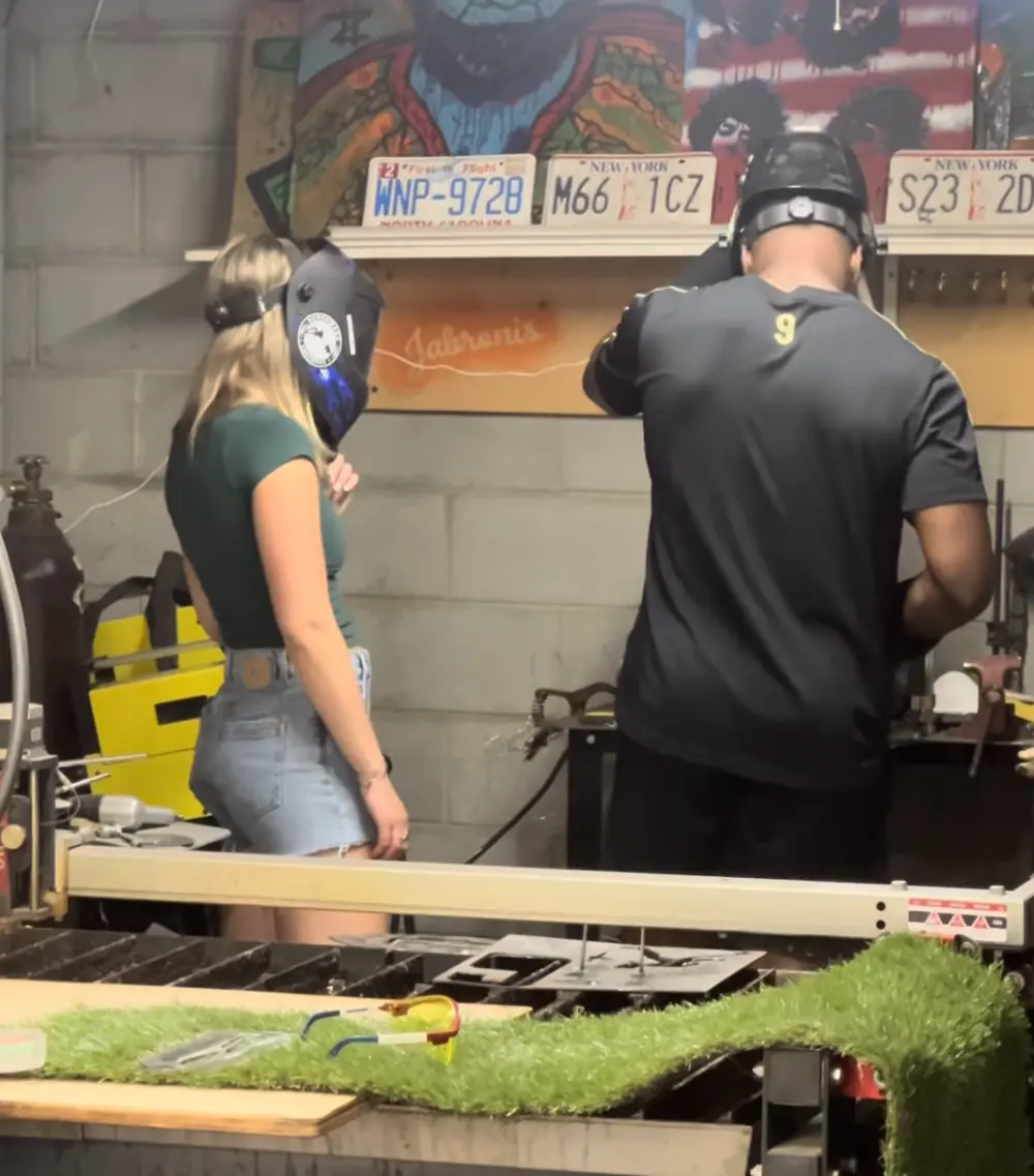 Two makers wearing welding helmets and working together at a shop bench